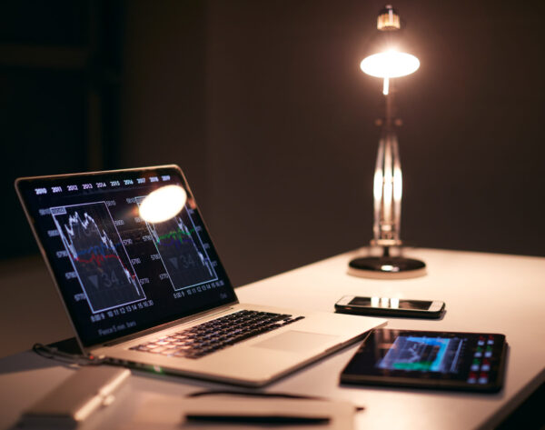 Desk Of  Share Trader At Desk With Stock Price Data Displayed On Laptop And Digital Tablet